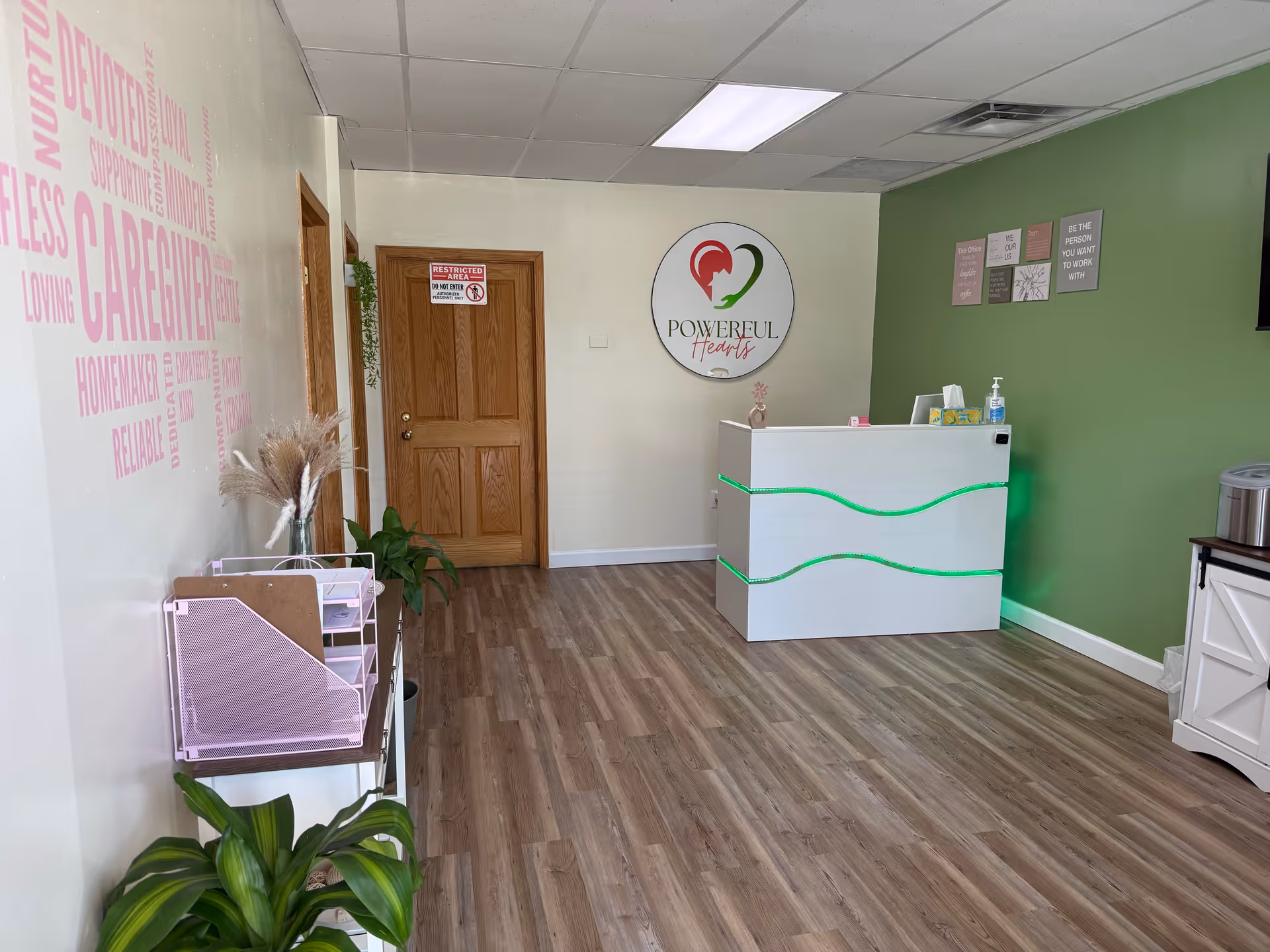Reception area of Powerful Hearts Home Care LLC with a white desk, green wall, and logo.