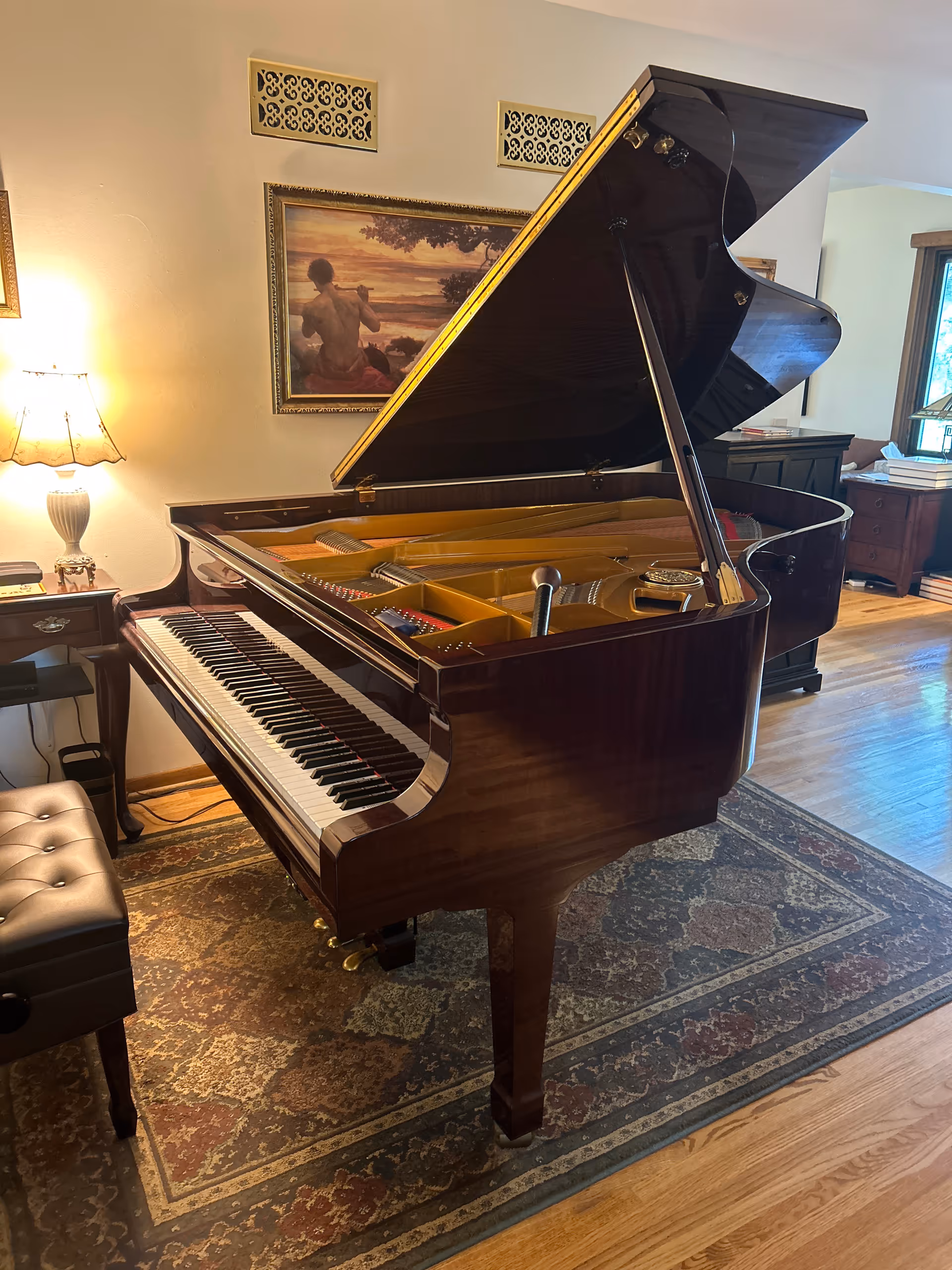 Polished grand piano in a cozy living room with lamp and framed artwork.
