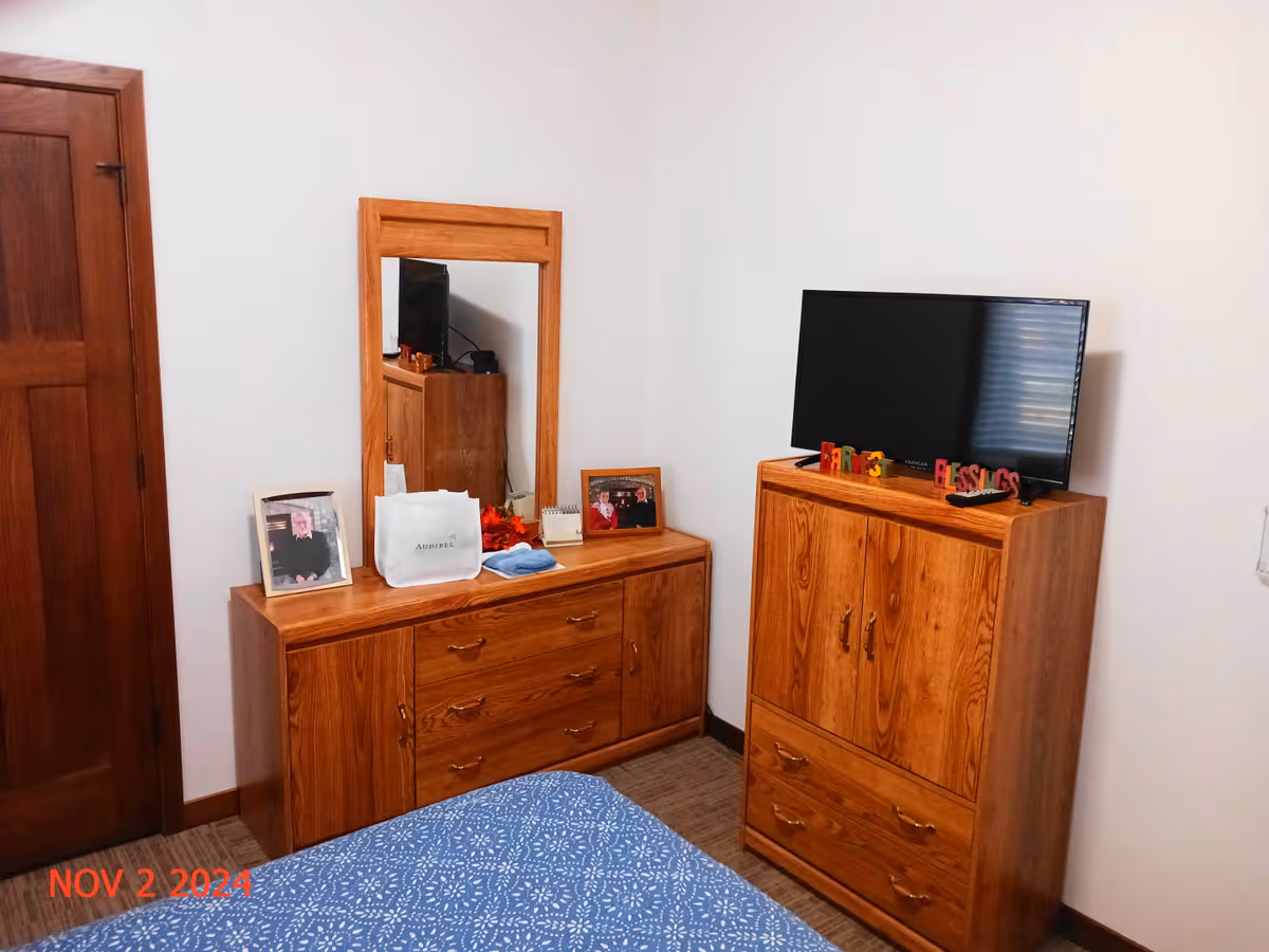 A tidy bedroom with wooden dressers, a mirror, and a TV on a cabinet.