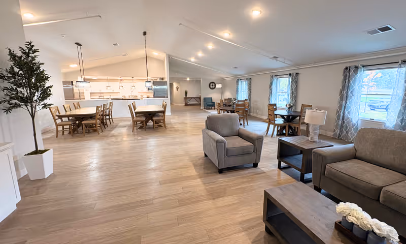 Bright, spacious senior living common area with dining tables, sofas, and large windows.