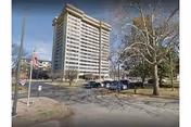 Tall multi-story senior living residence with parked cars and a flag in front.