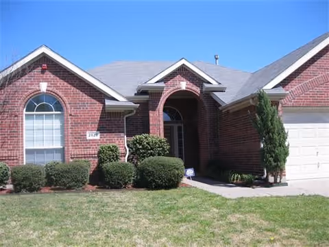 Brick single-story residential home with arched entryway, garage, and front lawn under a clear blue sky.