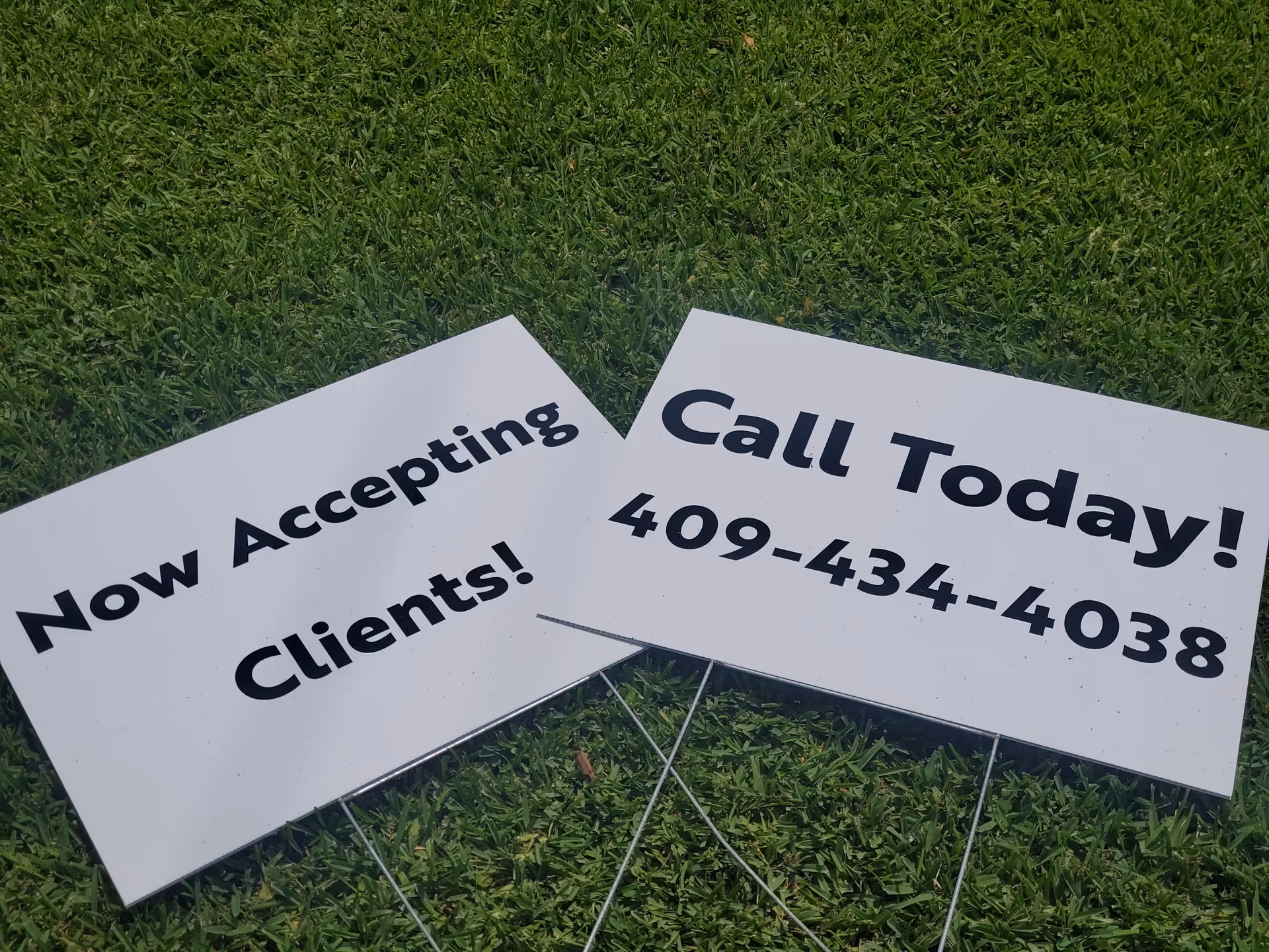 Two white yard signs on grass reading Now Accepting Clients! and Call Today!