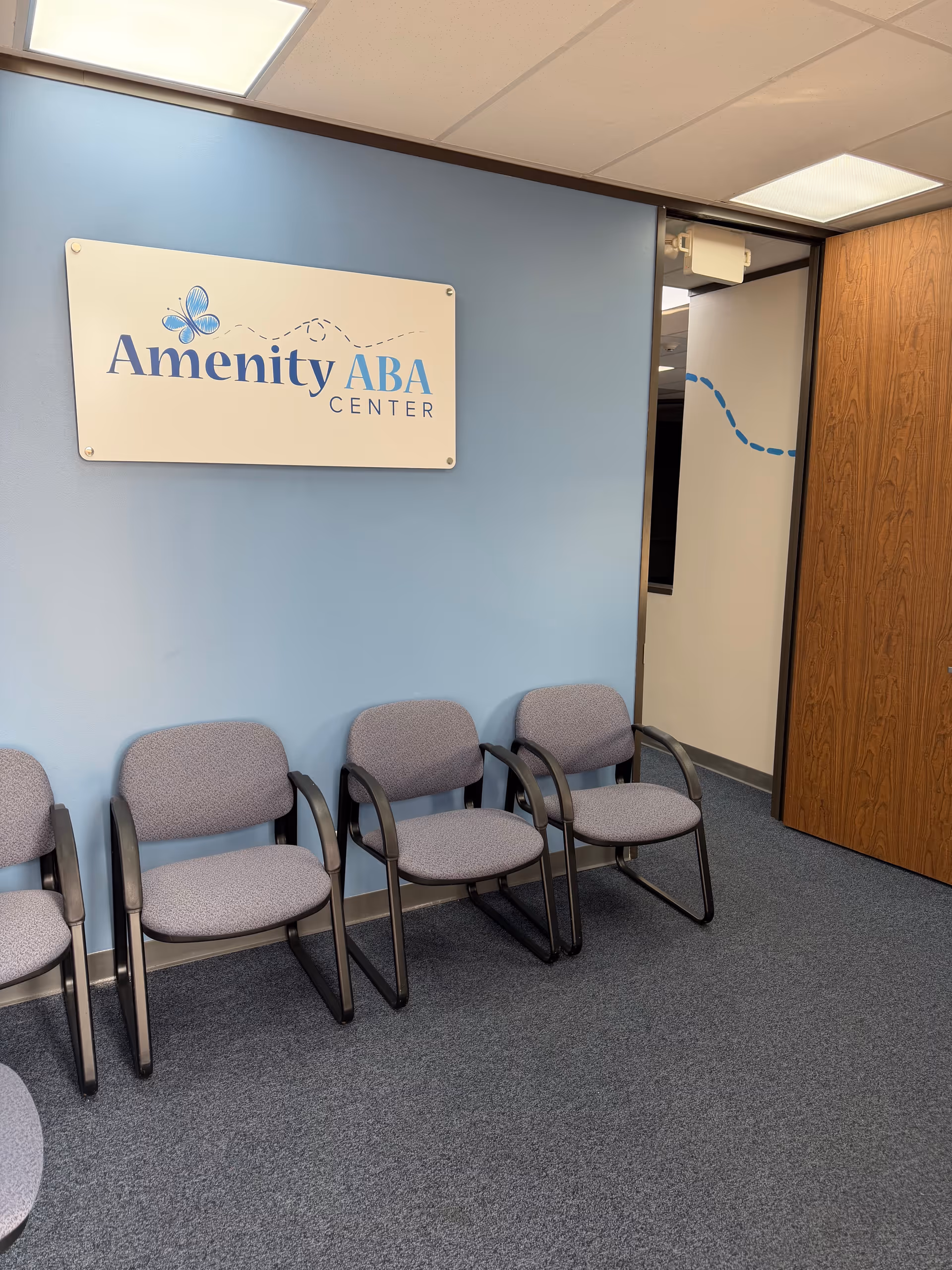 Blue-walled waiting area with row of gray chairs and an Amenity ABA Center sign.