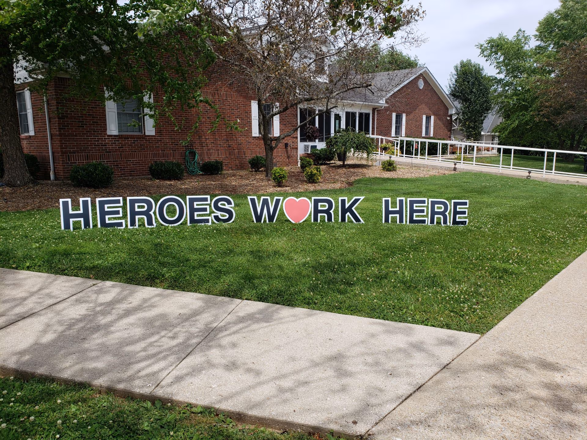 Brick-assisted living facility with a large lawn sign reading HEROES WORK HERE.