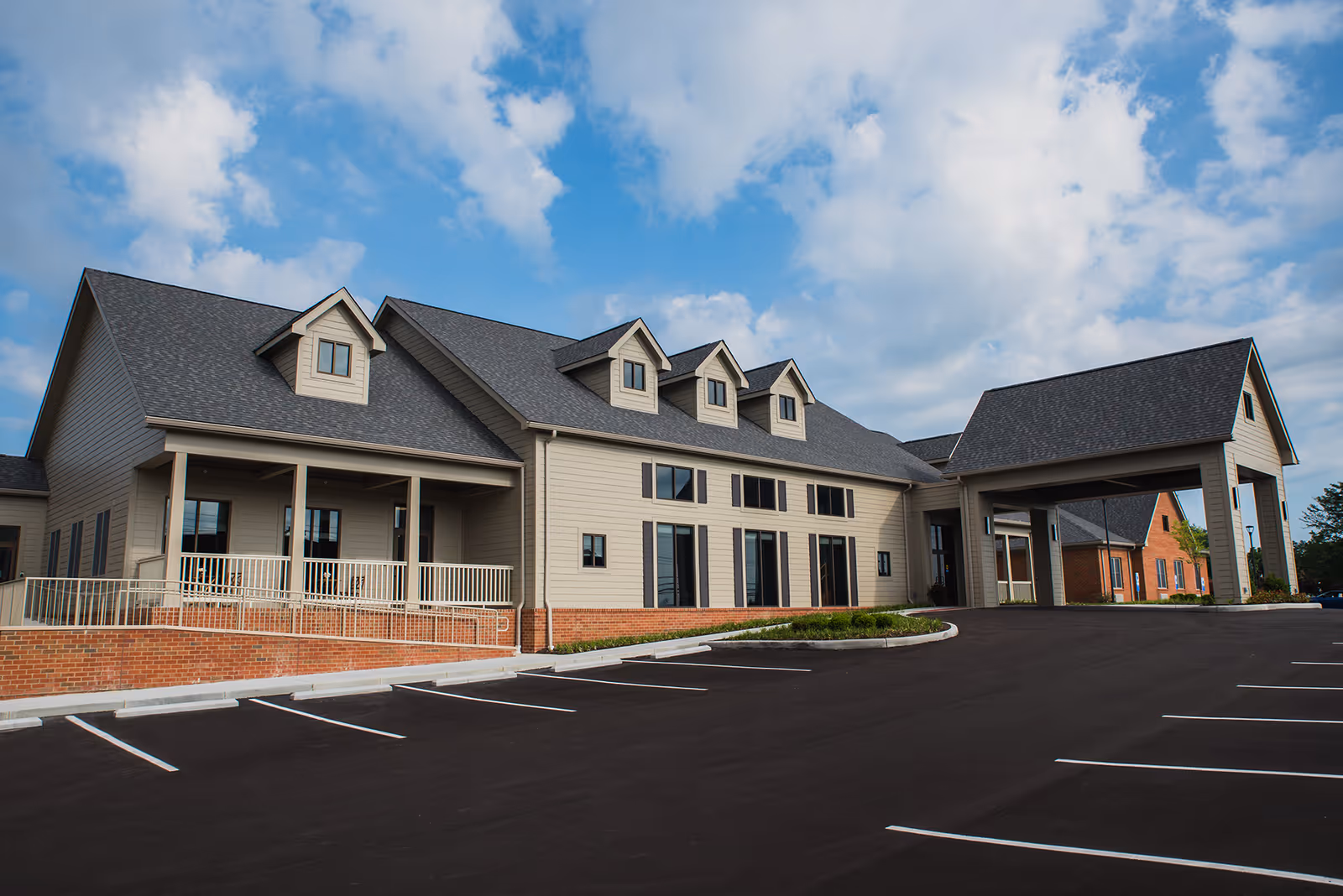 Modern senior living facility exterior with a covered entrance and expansive parking lot.