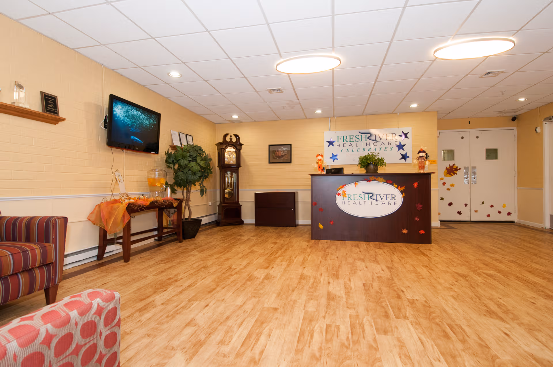 Reception lobby at Fresh River Healthcare with front desk, banner, clock, TV, plants, and seating.