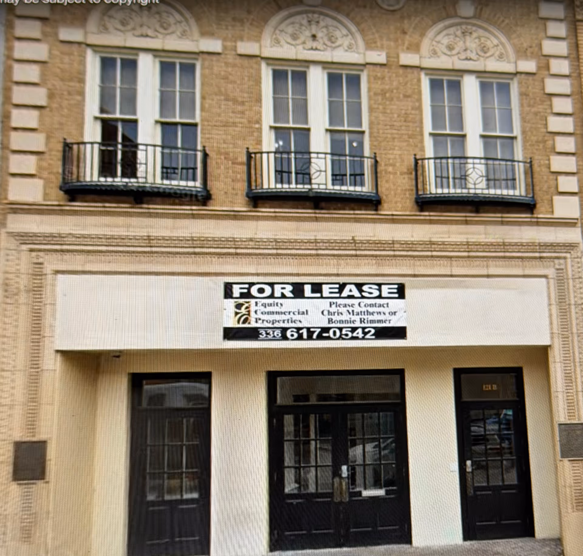 Three-story brick building with arched windows and a FOR LEASE sign above the entrance.