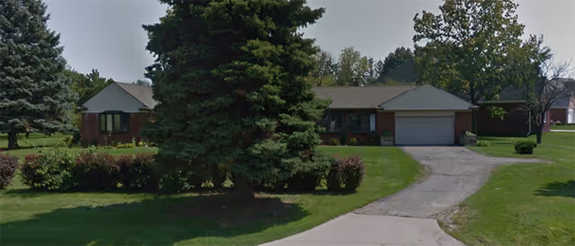 A single-story brick senior living facility with a driveway, garage, and manicured lawn.
