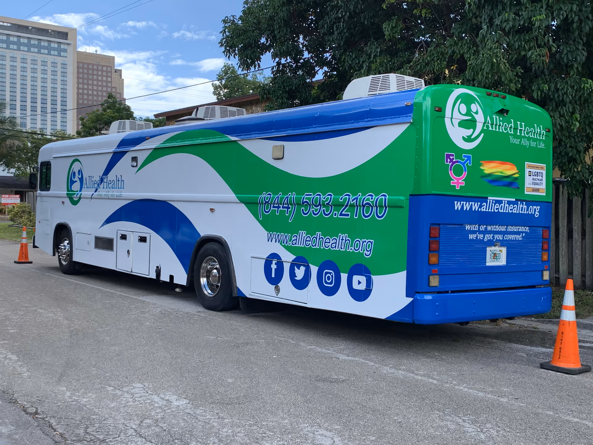 Large Allied Health-branded bus parked on a street with trees and orange traffic cones.