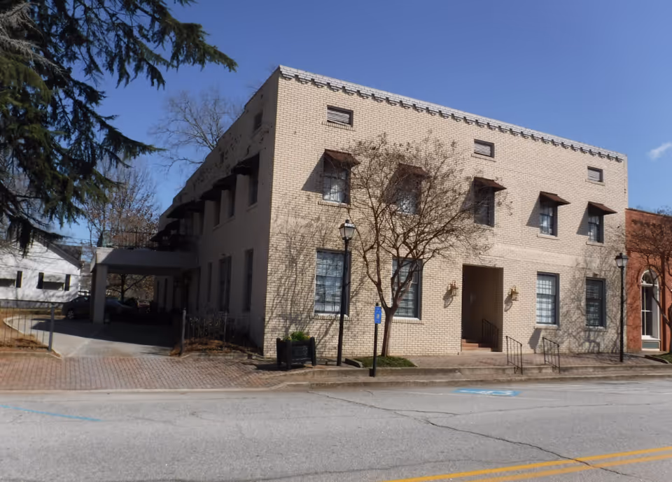 Two-story beige brick senior living building with entrance and street view.