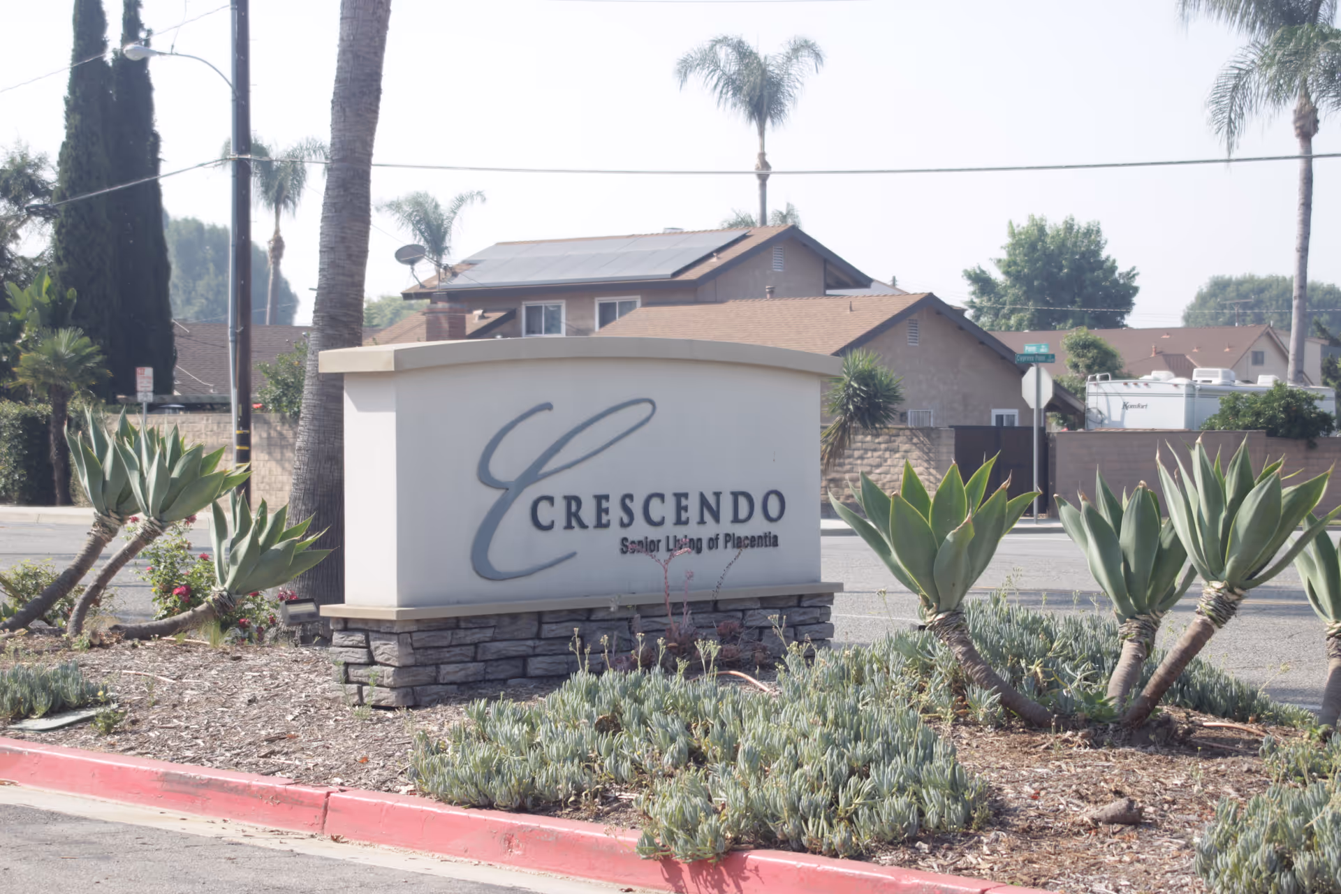 Exterior view of Crescendo Senior Living sign with desert plants and street behind.