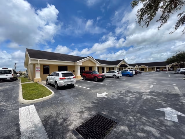 Single-story beige senior living facility with a row of entrances and parked cars in a lot.