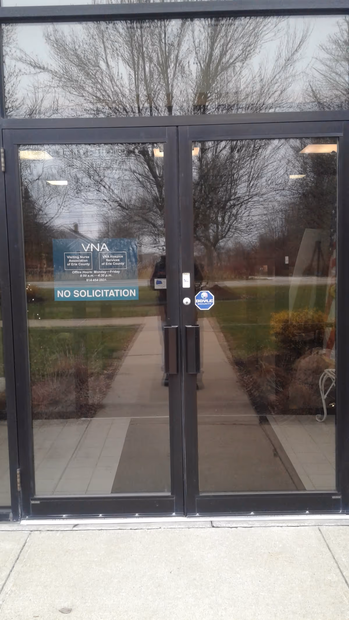 Glass double doors with reflections of trees and sidewalk, no people visible.