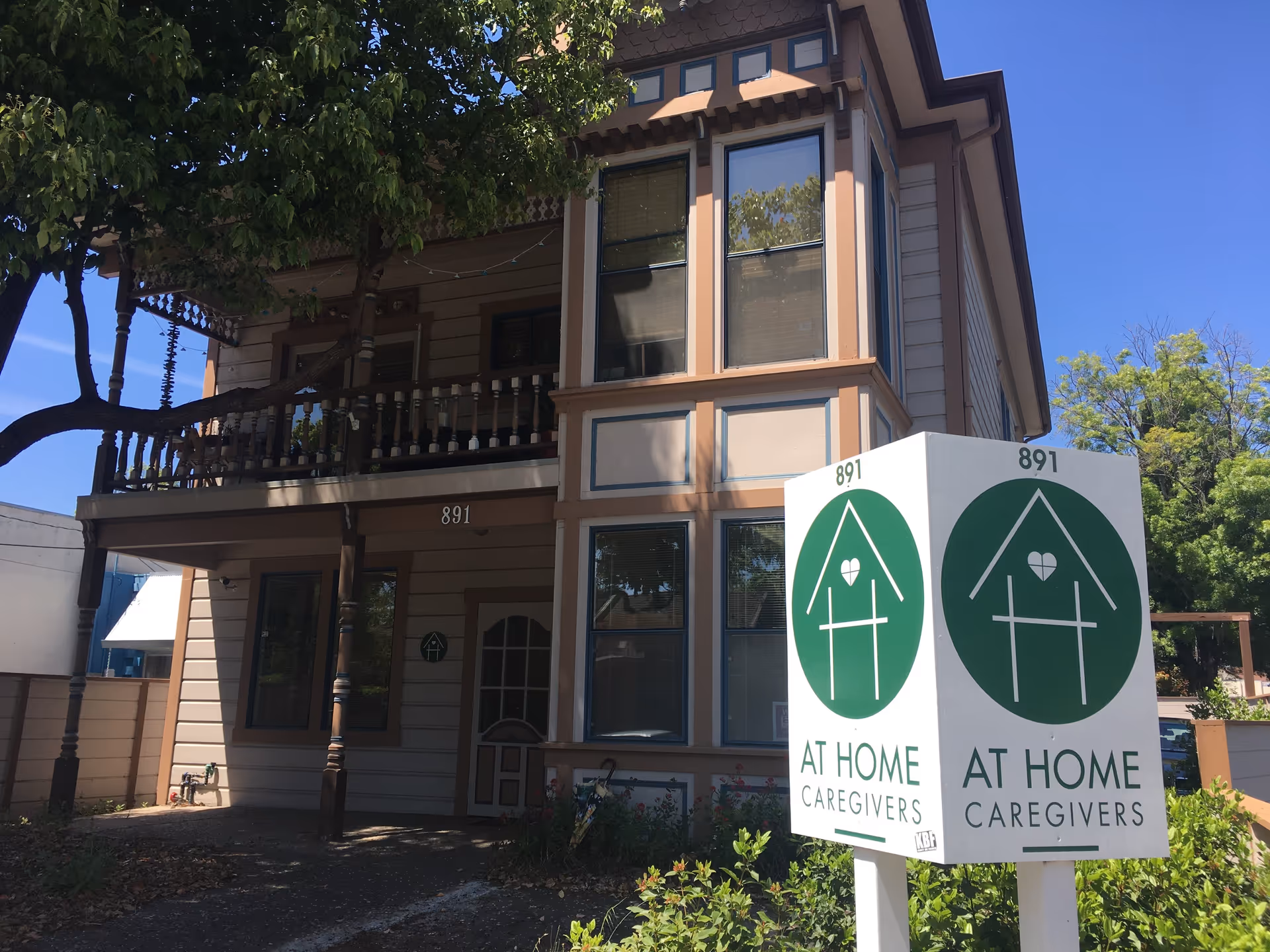 Two-story beige building with a large green At Home Caregivers sign.