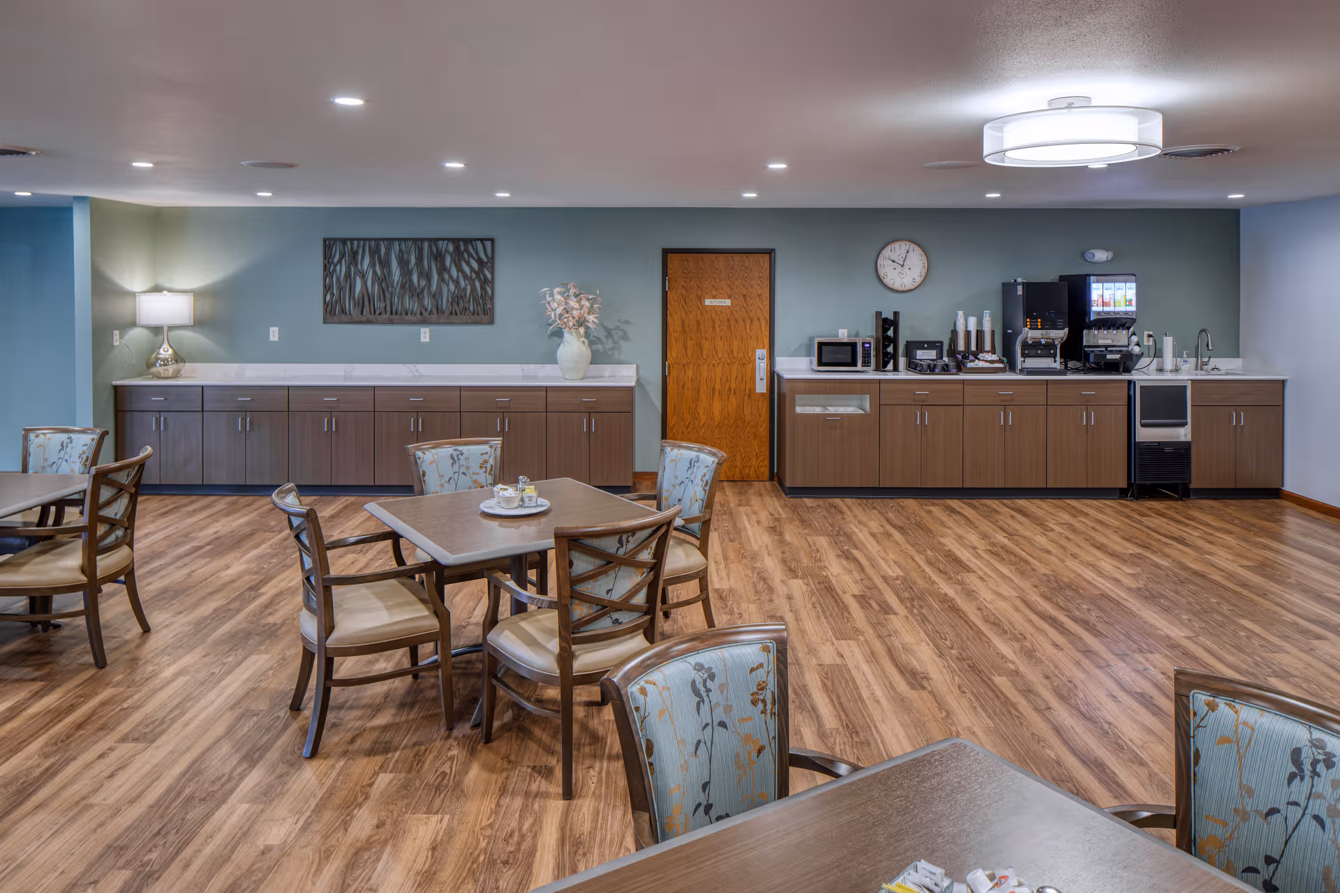 Interior dining room with wooden floors, tables and chairs, and a beverage station along back wall.