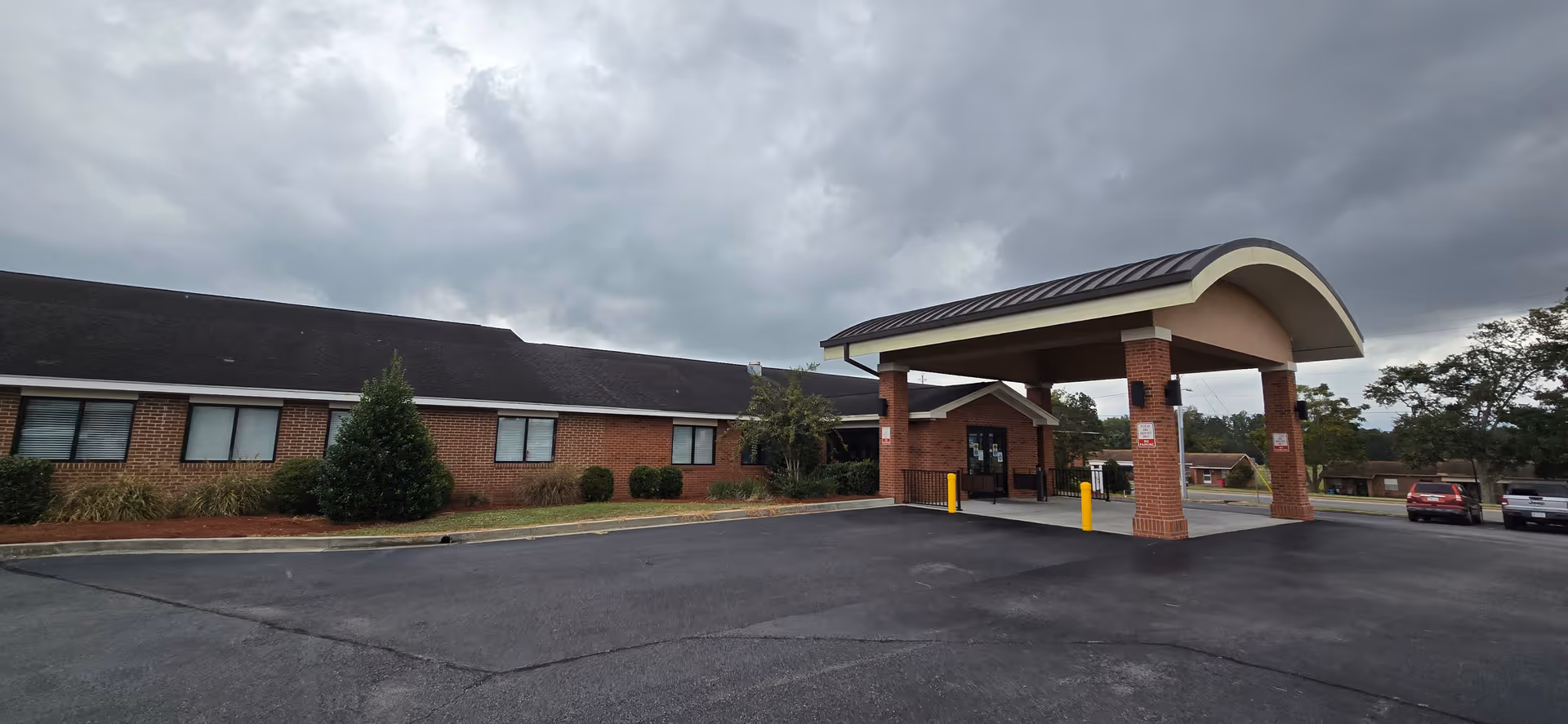 Brick building with curved-roof entrance canopy and parking in front.