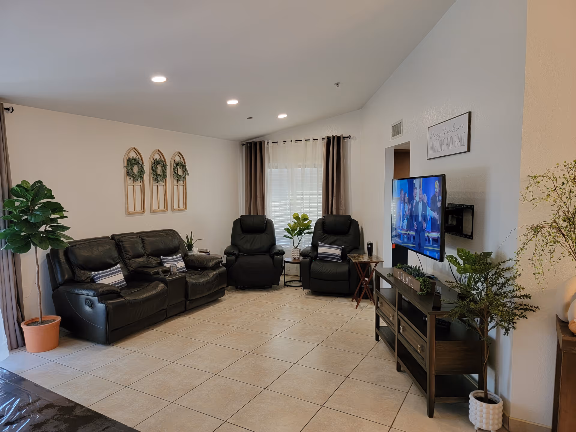 Cozy senior living lounge with black leather seating, TV, and plants.