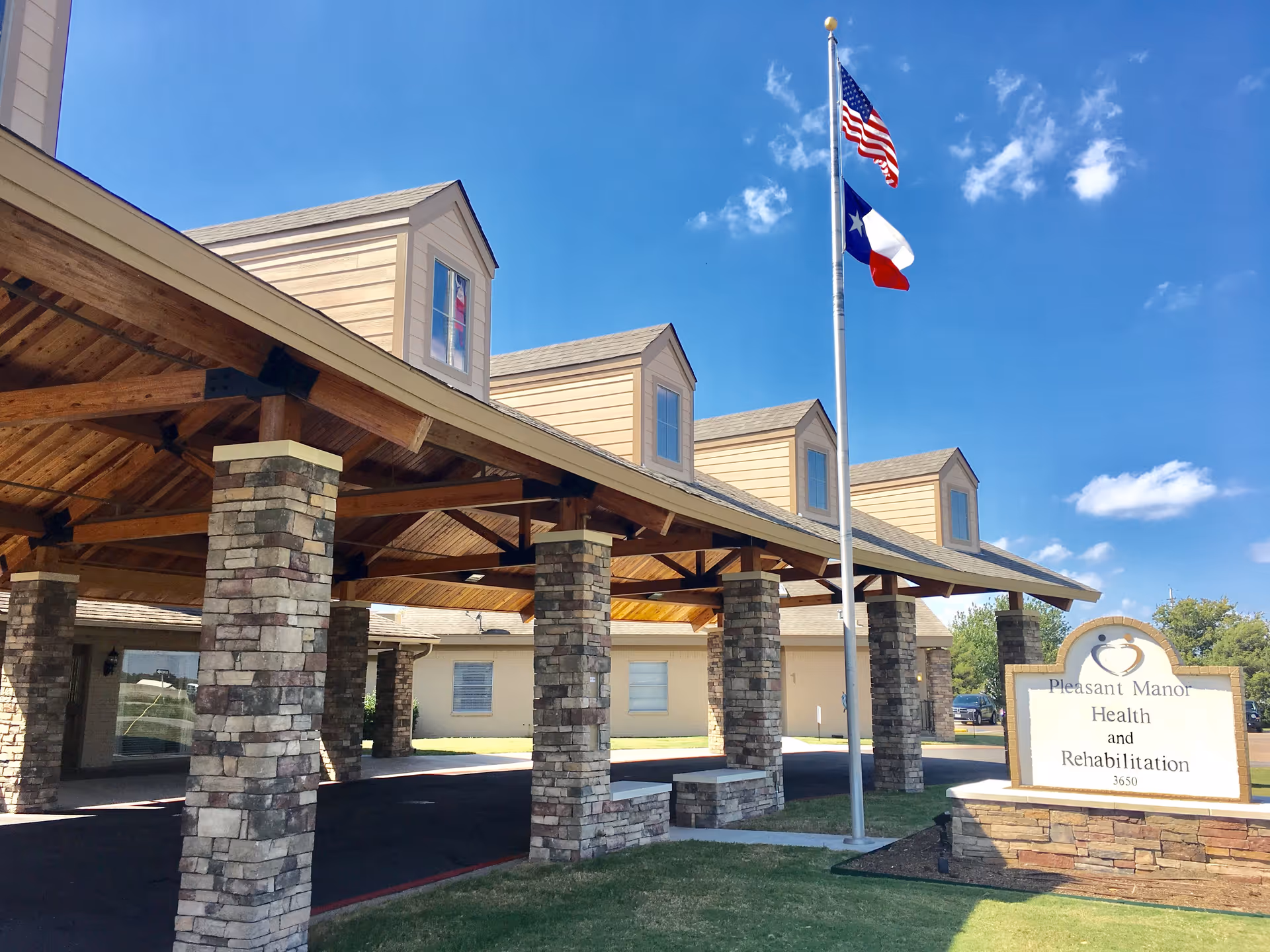 Front entrance of Pleasant Manor Health and Rehabilitation Center with stone pillars and flags.