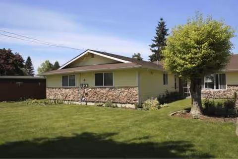 Single-story green building with stone veneer, lawn and trees in front.