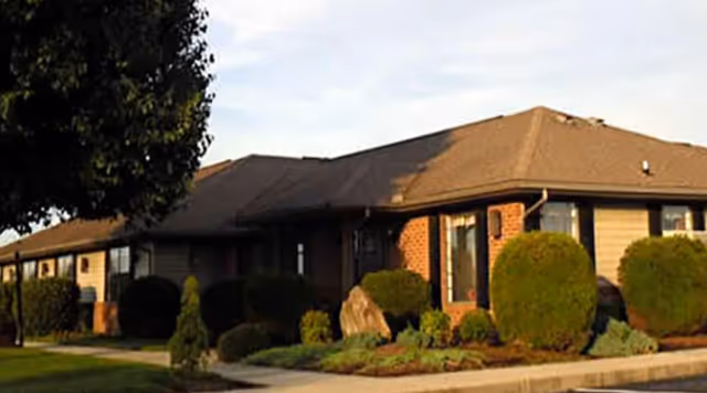 Single-story brick assisted living building with manicured shrubs and sidewalk.