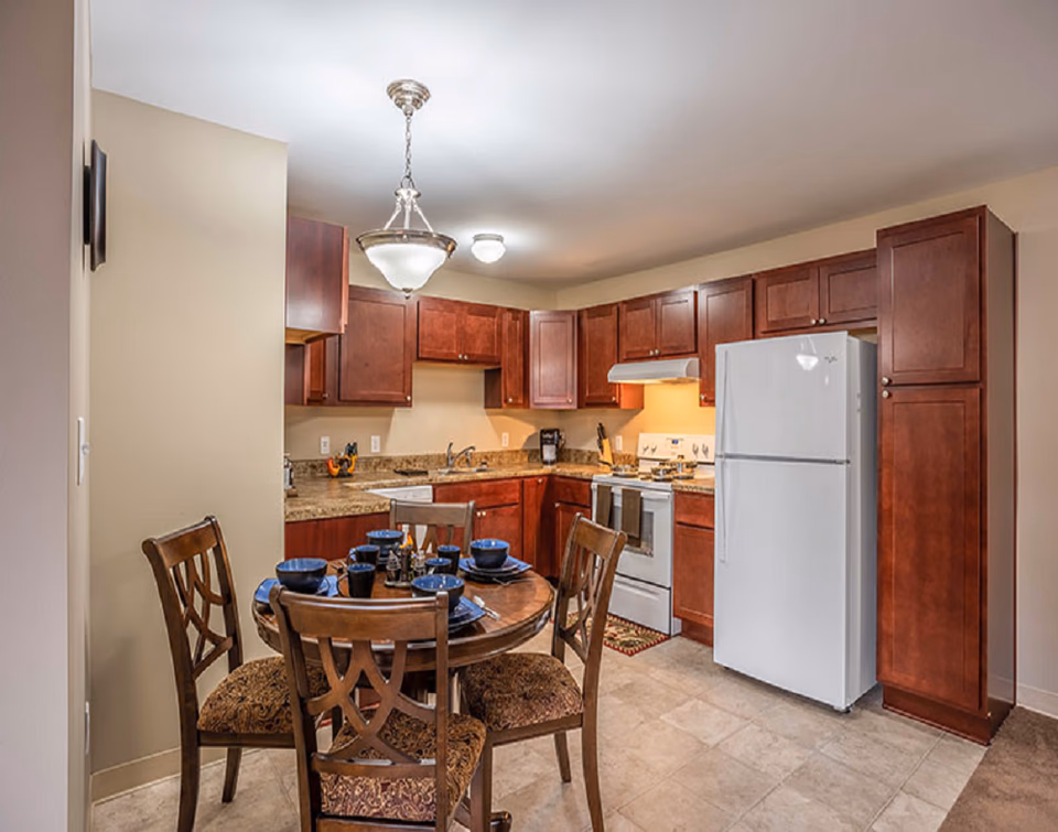Bright kitchen with dark wood cabinets, white refrigerator, stove, and round dining table.