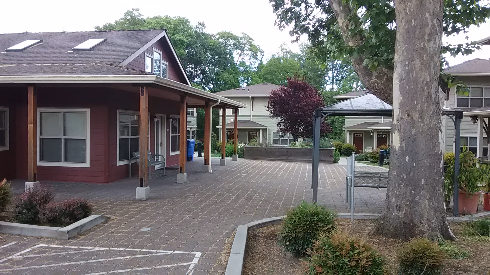 Exterior view of Cedars senior living with a red building, paved courtyard, and trees.