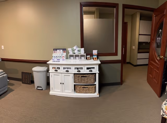 A white cabinet with baskets and supplies sits in a beige common room.