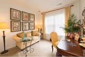 Cozy senior living lounge with sofa, desk, plants, and framed art.