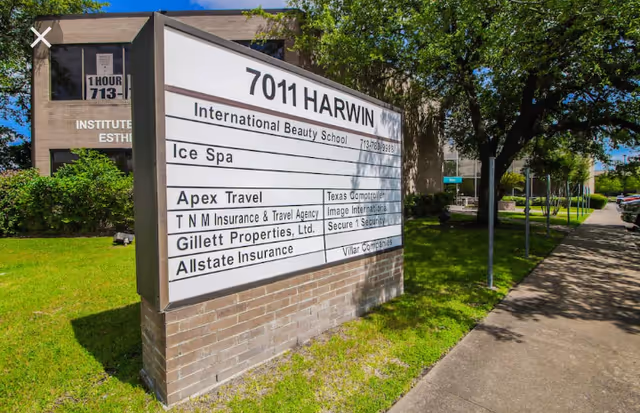 Exterior signboard for multiple businesses beside a sidewalk and green lawn.