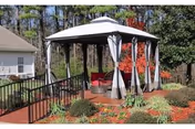 Outdoor gazebo with draped curtains and seating, surrounded by landscaped garden near a building.
