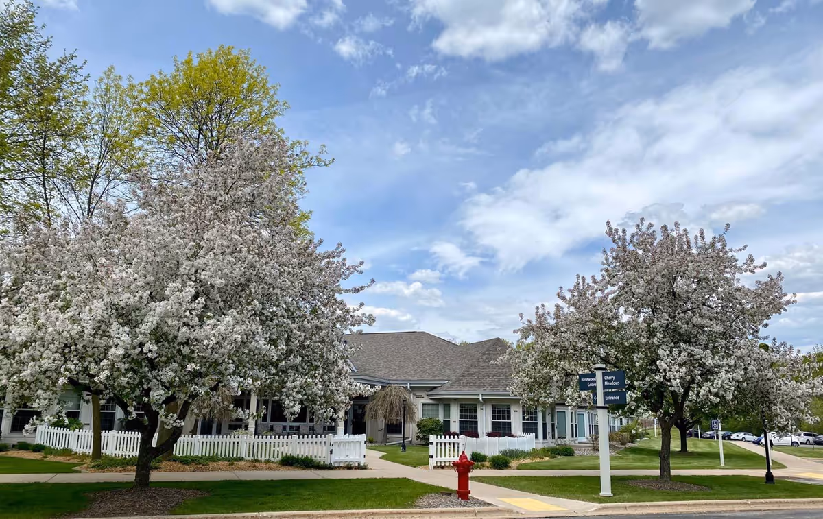 Front view of a single-story hospice with blooming cherry trees and a white picket fence.