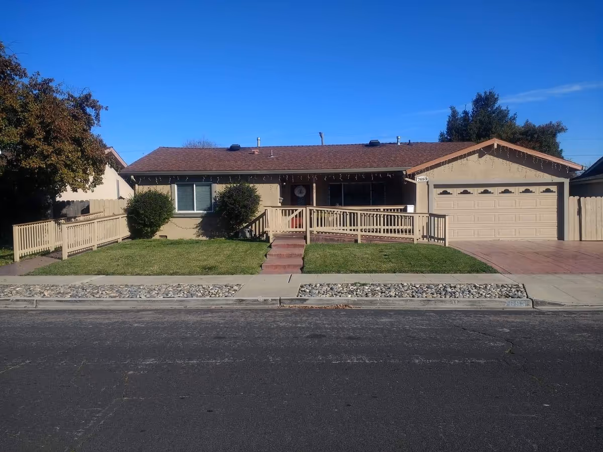 Single-story beige senior residence with front porch, railing, and attached two-car garage.