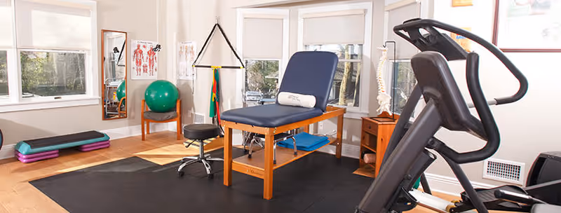 An interior physical therapy room with a treatment table, treadmill, mats, and equipment.