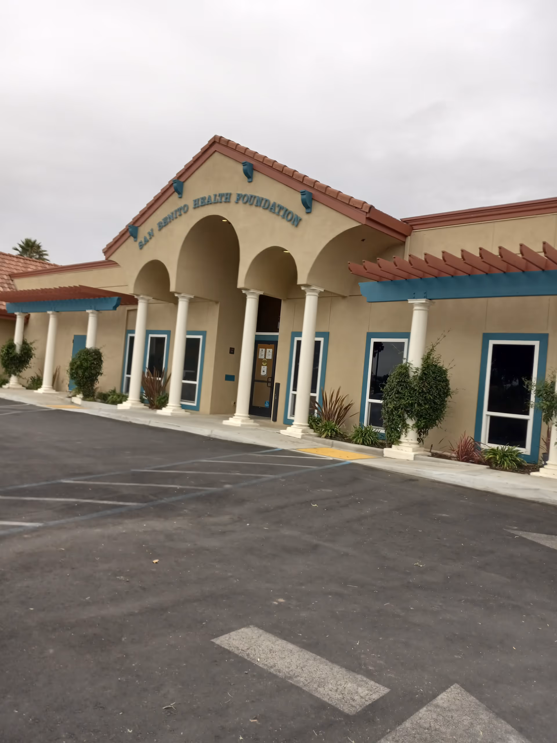 Exterior view of San Benito Health Foundation building with arched entrance and parking.