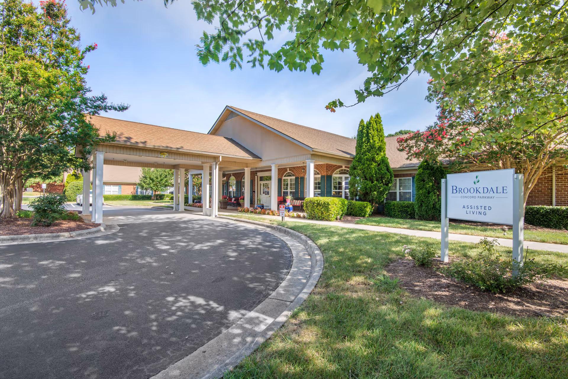Curved driveway leads to Brookdale Concord Parkway entrance with landscaping and a sign.
