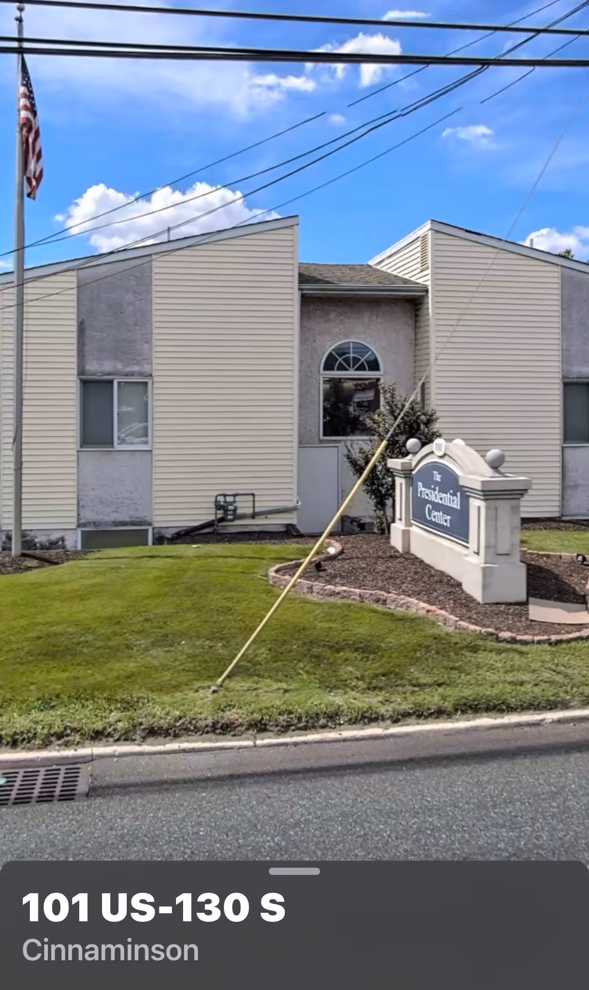 Exterior view of a beige building with a sign and flag at the front.