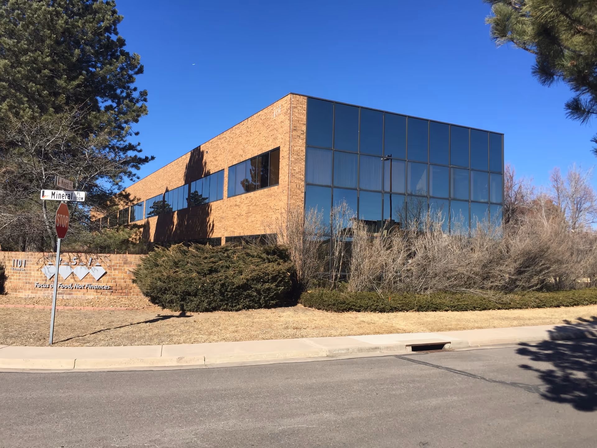 Modern brick building with large glass front windows and surrounding sparse landscaping along a street.