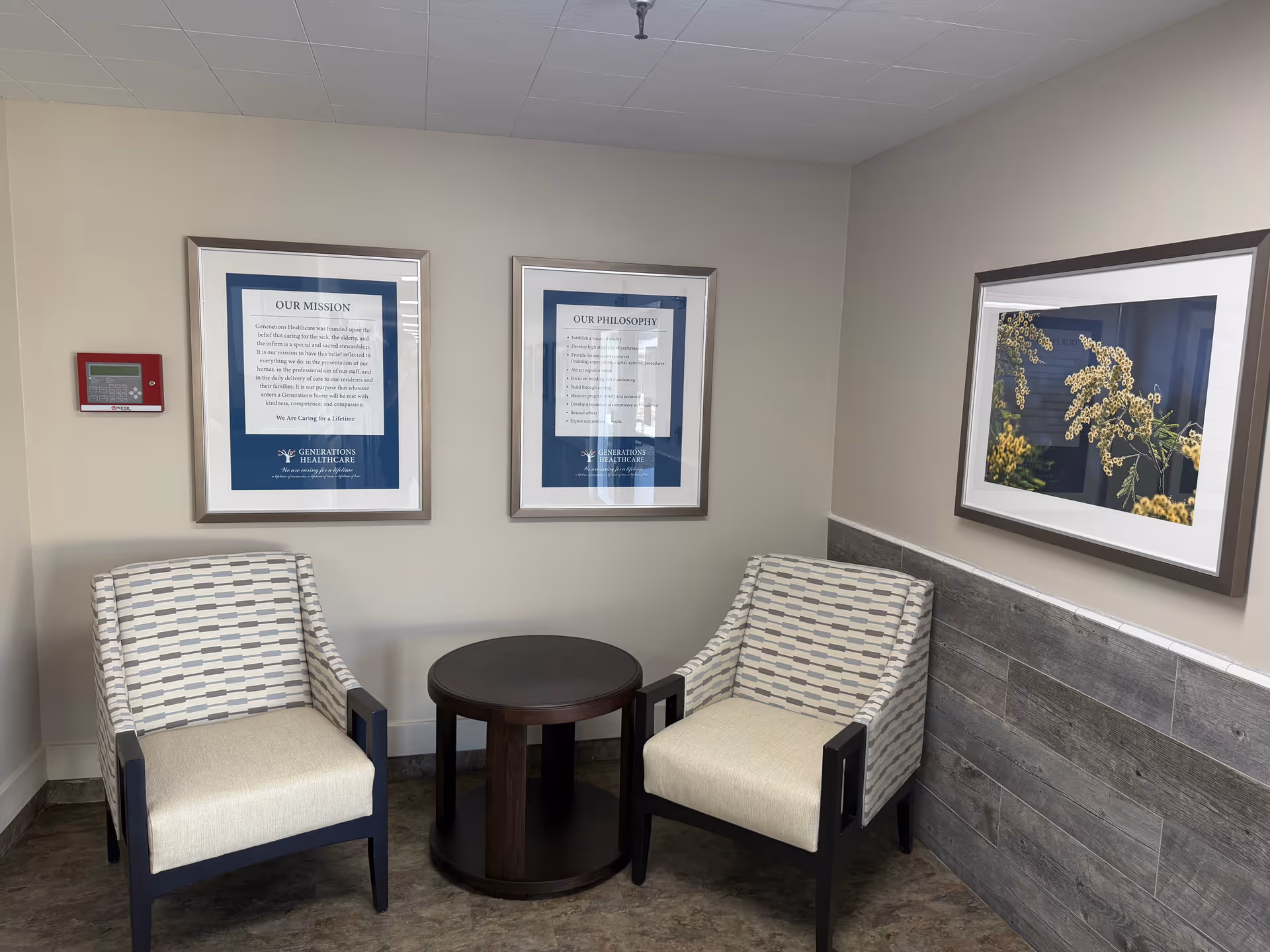 Two striped armchairs with round table in a small lobby area of a senior care facility.