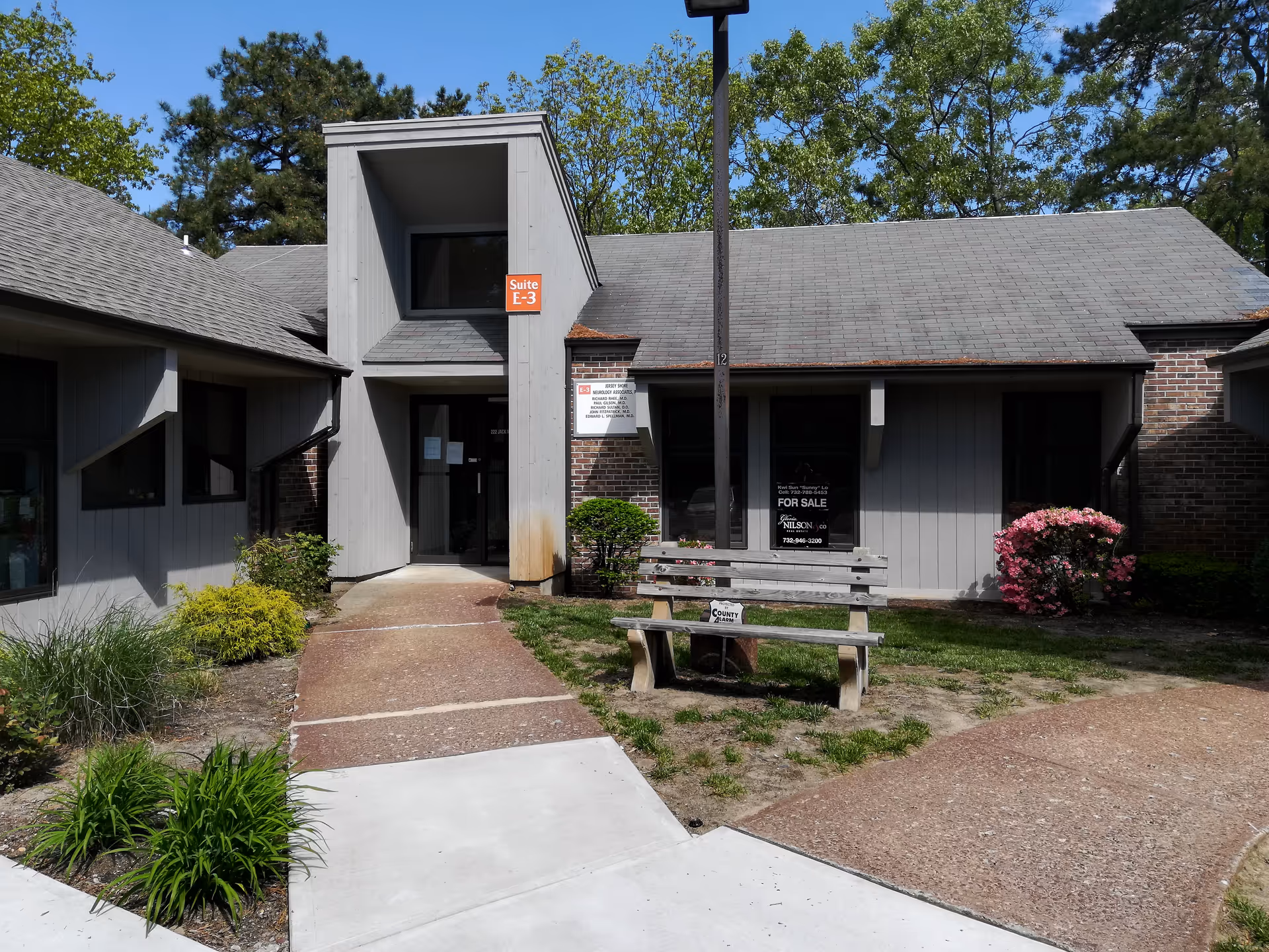 Front view of a gray low-rise building with a walkway, bench, and shrubs.