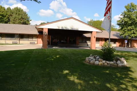 Front view of a brick nursing facility with a covered entrance and flagpole.