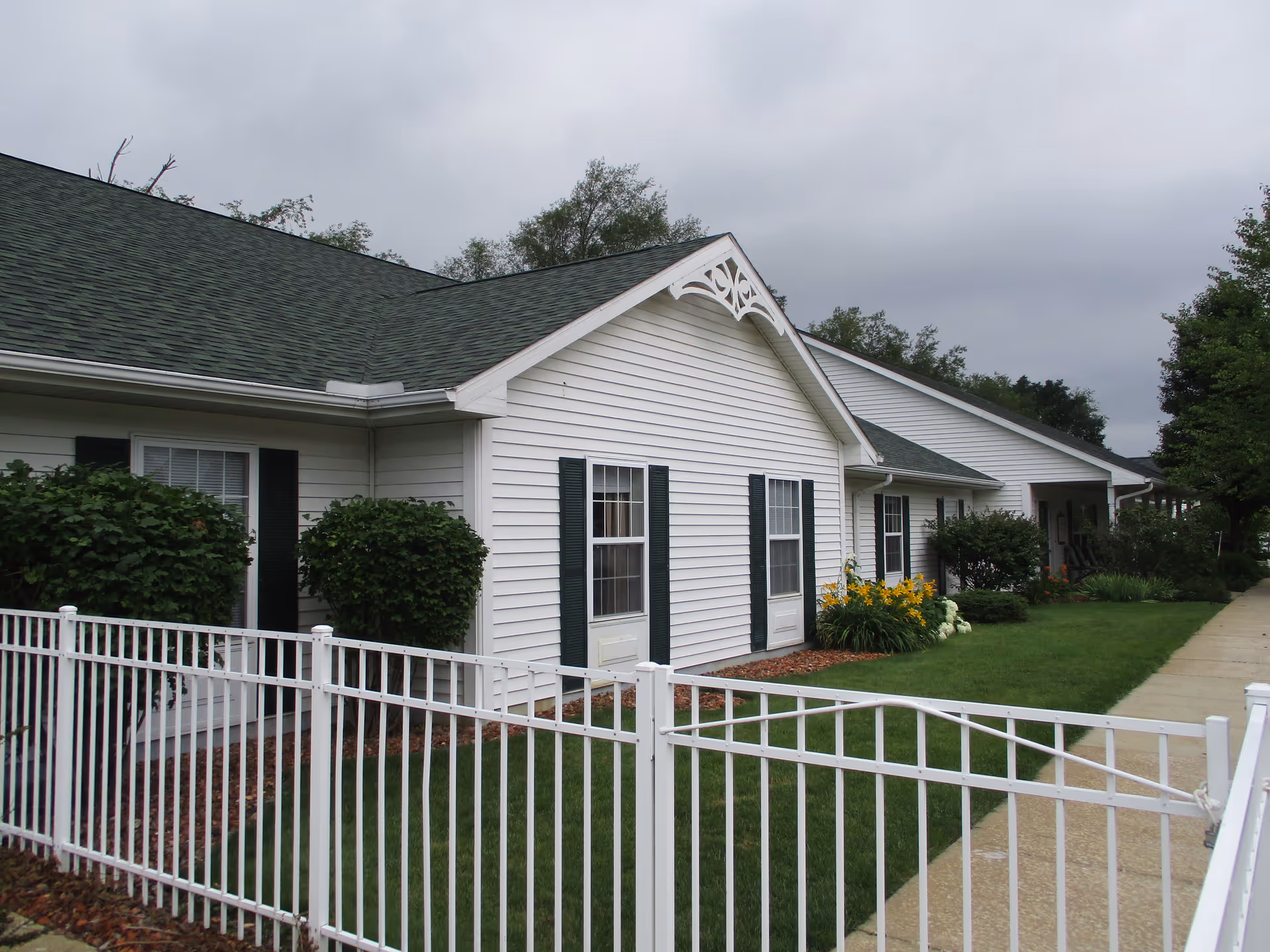 Exterior of Tecumseh Place: a white, single-story building with green shutters and a white fence.