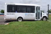 White shuttle bus parked on grass beside a road with Stamford branding.
