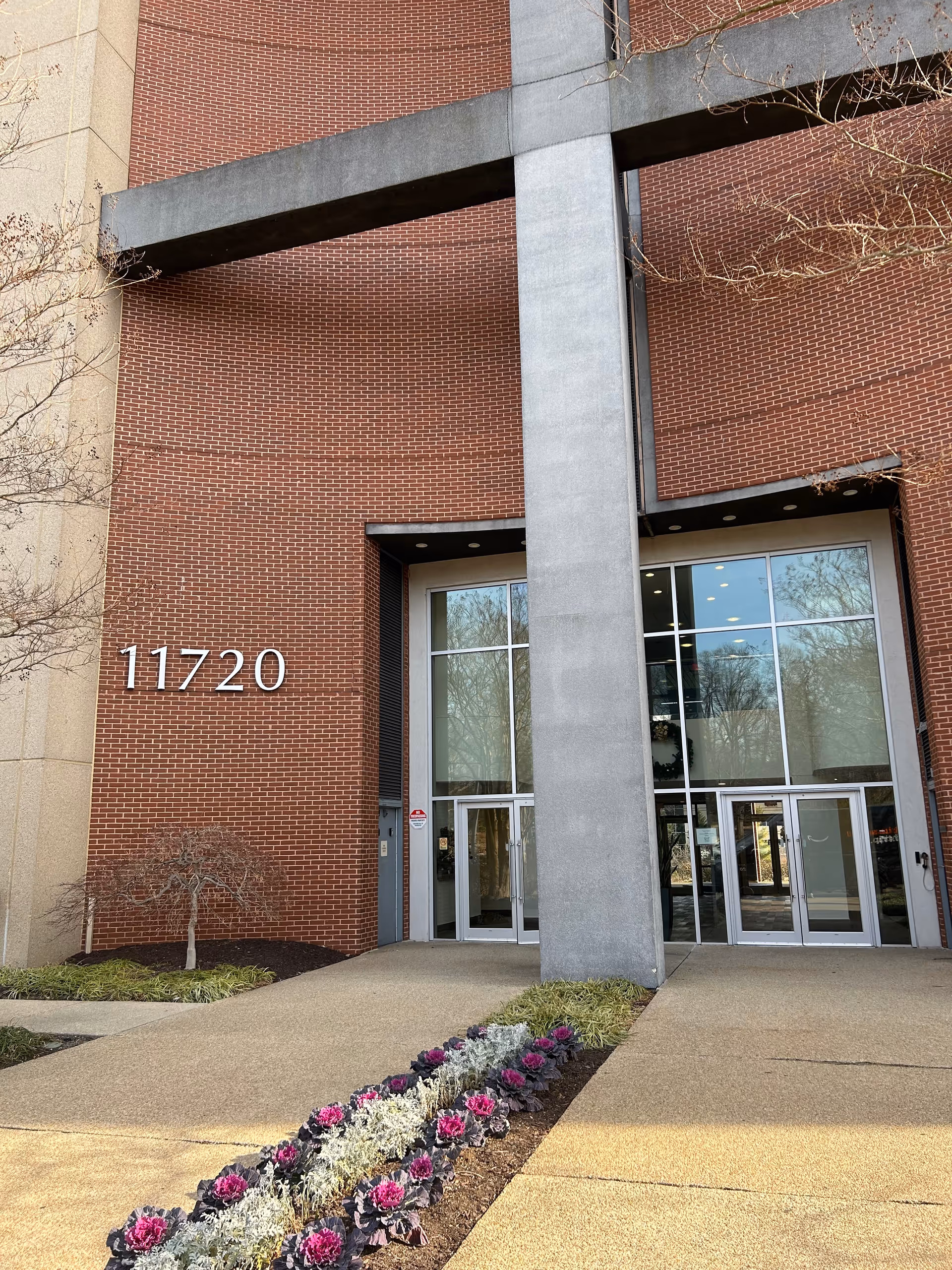 Brick building entrance with large glass doors and a flower-lined walkway.