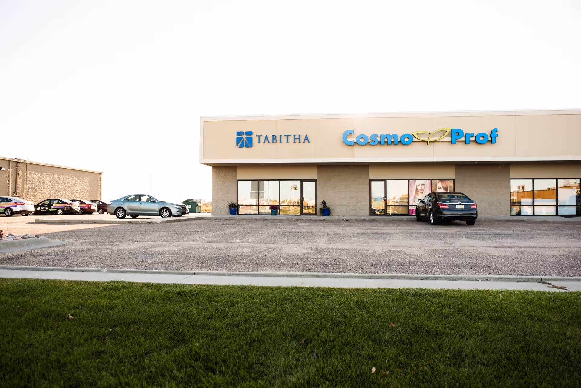 Exterior view of a single-story building with CosmoProf signage and cars in the lot.