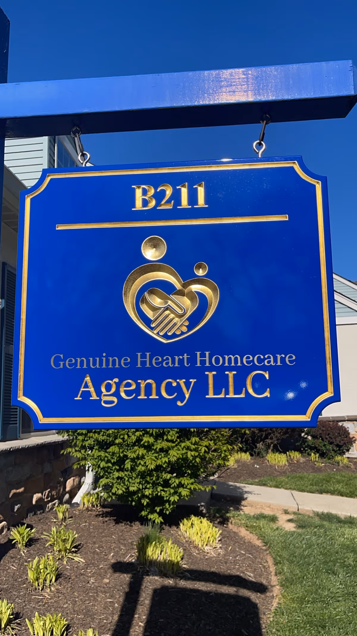 Bright blue hanging sign displays Genuine Heart Homecare Agency LLC outside a building.