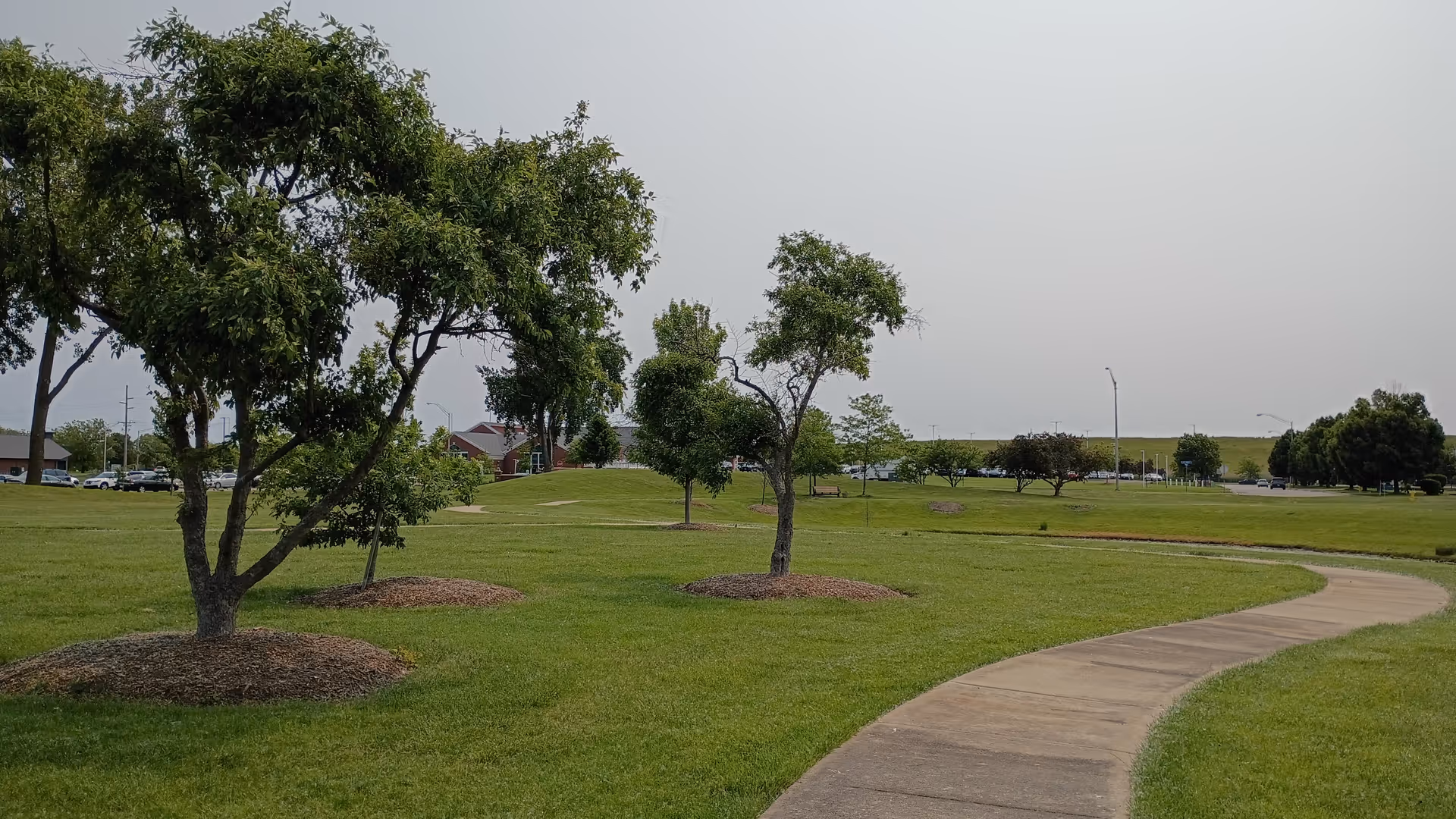 Curved concrete path winds through a grassy park with scattered trees at Hartsfield Village.