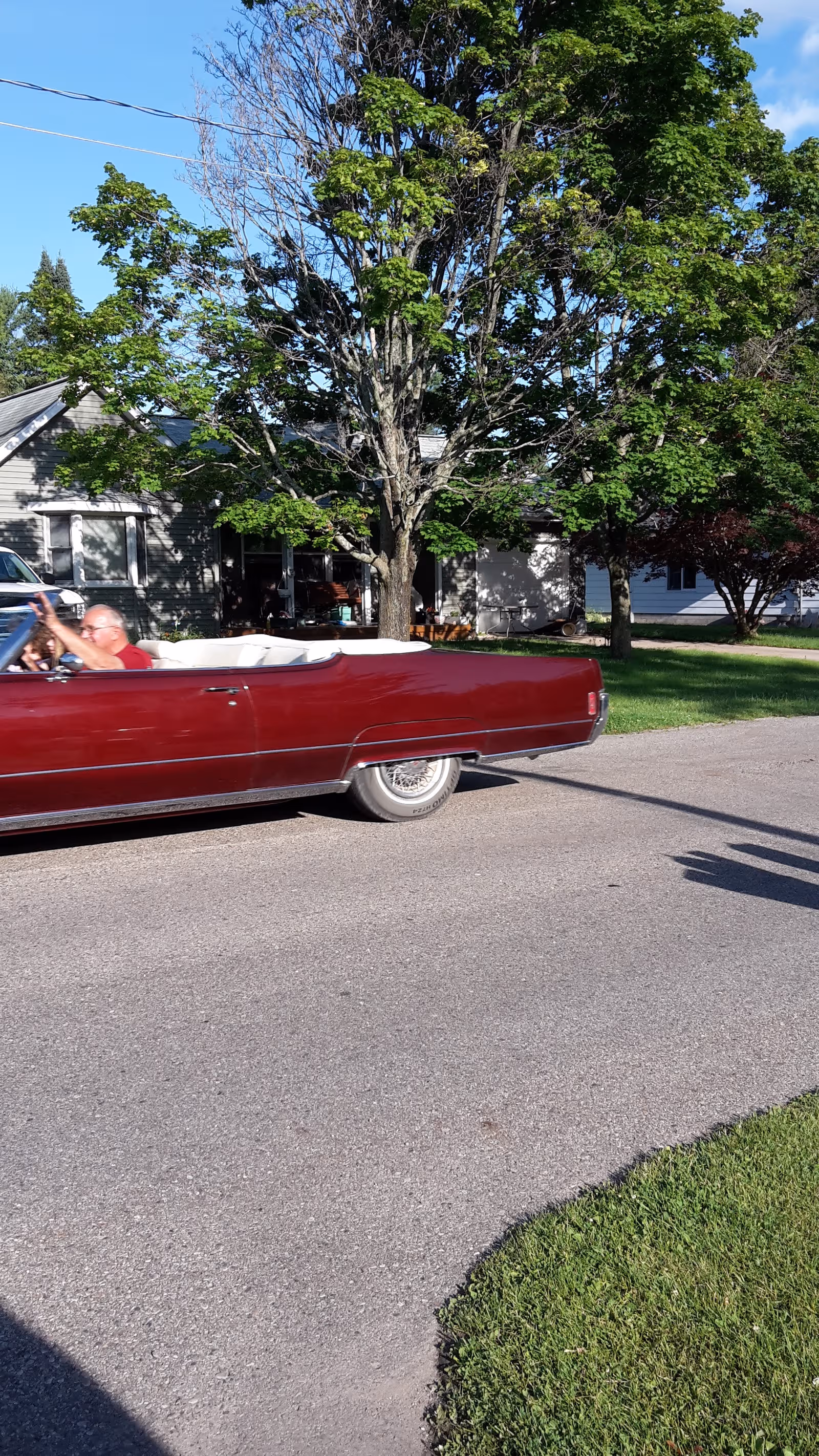Red convertible car on a residential street with trees and houses in the background.