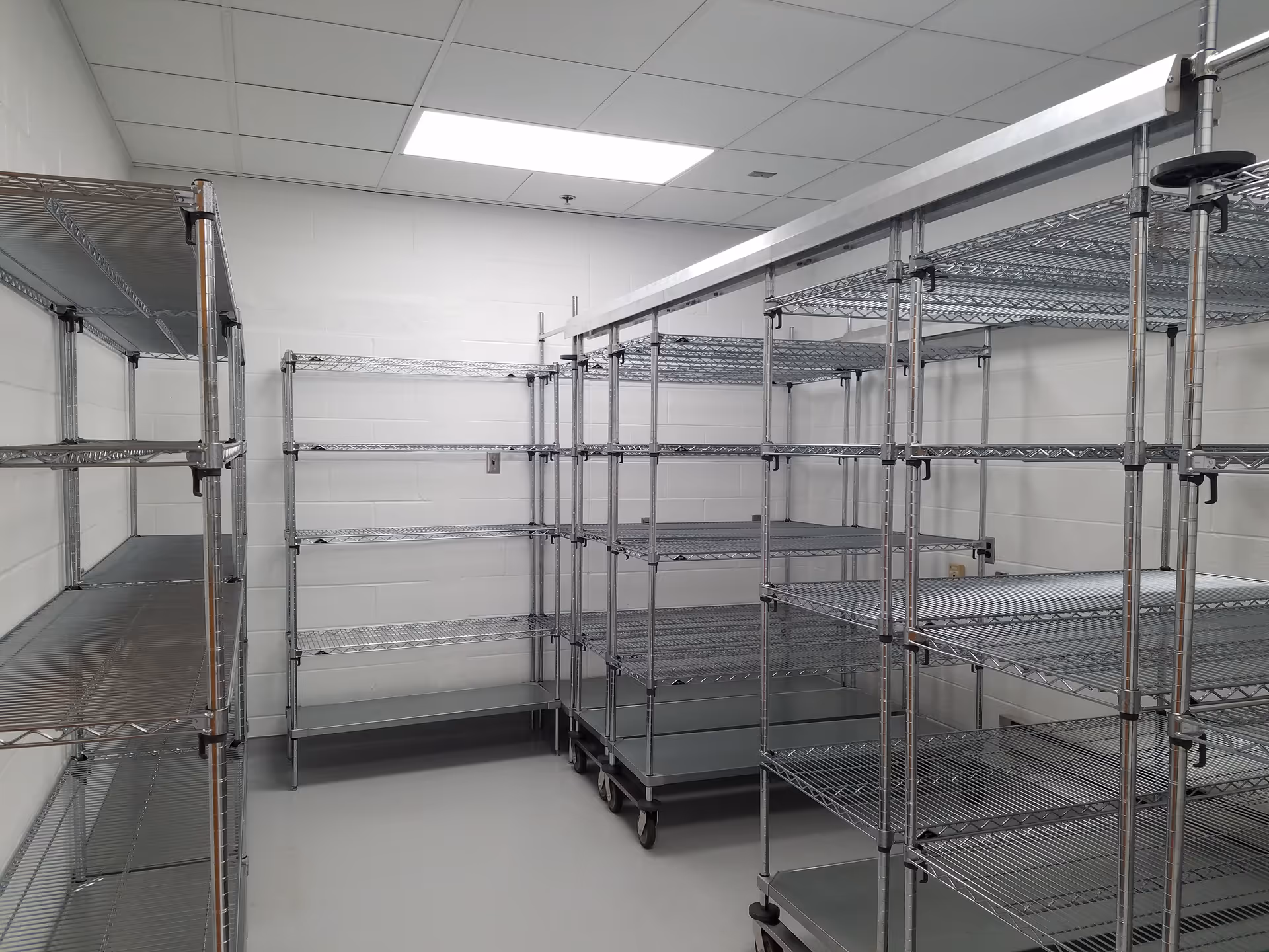 Industrial storage room with empty metal wire shelving on wheels along white cinder block walls.