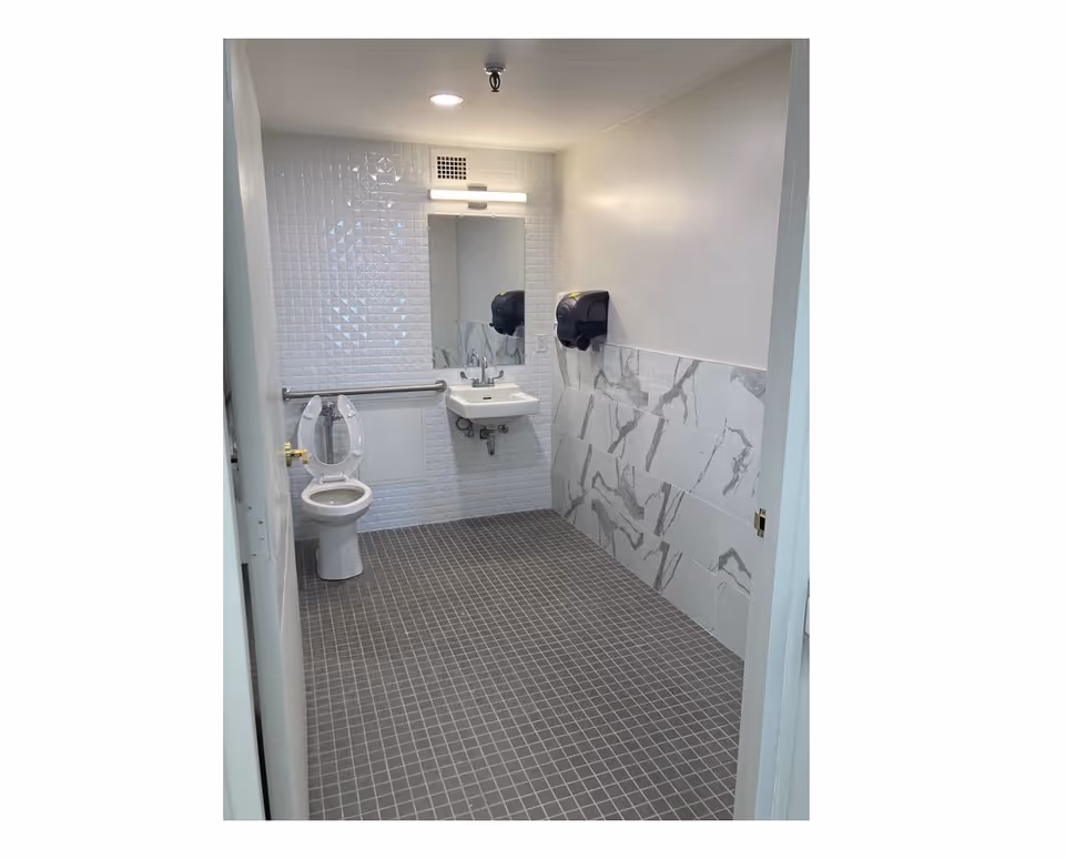 Compact senior facility bathroom with toilet, sink, mirror, and grab bar.